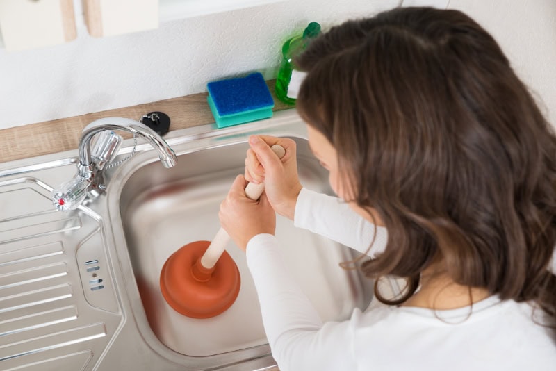 Person using a plunger to clear clogged sink.
