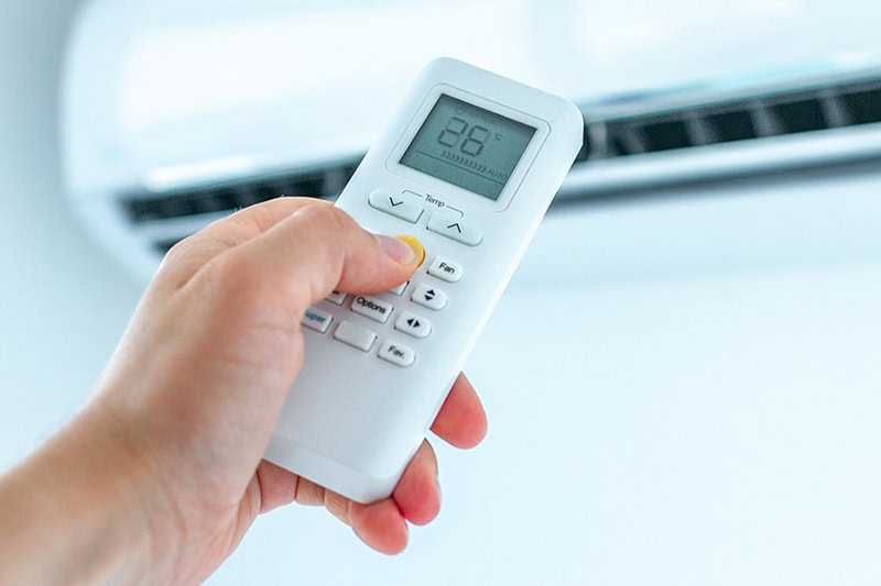 Air conditioner temperature adjustment with remote controller in room at home.